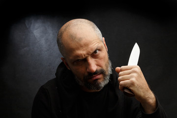 Portrait of a bald man with a beard with a knife on a dirty gray background. Maniac.