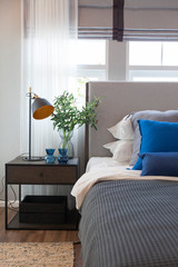 Modern bedroom in minimalist white and blue interior tone with with comfy pillow, side table and table lamp. 