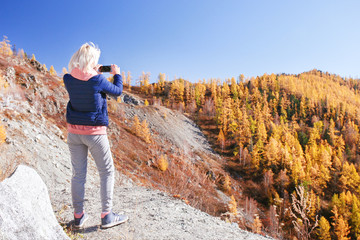 Woman blogger taking photo by smartphone in mountains. Blogger updates content.