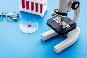 Blood testing laboratory. Samples viewing under microscope near tubes on blue background top view space for text