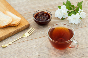 Glass cup of tea, bread, strawberry jam and white jasmine flowers