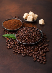 Fresh raw organic coffee beans with ground powder and cane sugar cubes with coffee trea leaf on brown background.