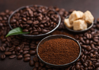 Fresh raw organic coffee beans with ground powder and cane sugar cubes with coffee trea leaf on brown background.