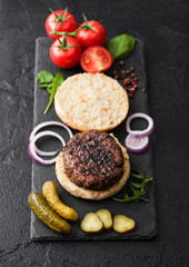 Fresh grilled minced pepper beef burgers on stone chopping board with buns onion and tomatoes on black background. Salty pickles and basil