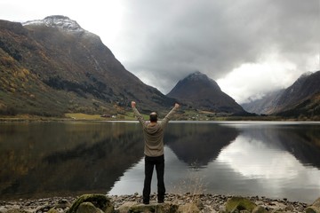 happy man raising his arms to the sky in beautiful Norwegian mountain lake scenery