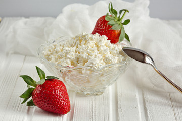 White bowl with fresh red ripe strawberries and natural cottage cheese, on white wooden table for fitness breakfast. Dietary product. The concept of healthy eating.