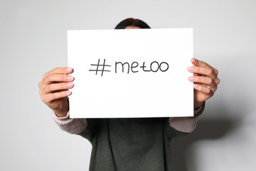 Young woman holding #METOO card against light background