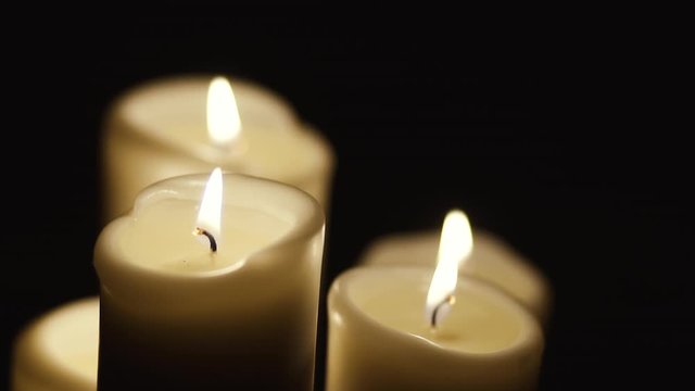 Static view of four lit candles, slow motion of the flames on the candles, the candles stand against a dark background