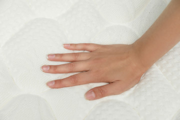 Young woman touching modern orthopedic mattress, closeup