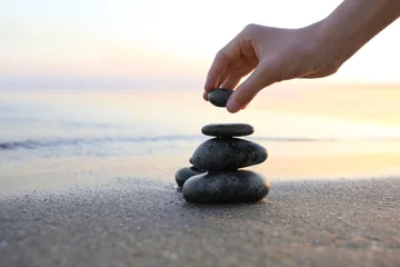 Photo sur Aluminium Pierres dans le sable Femme empilant des pierres sombres sur le sable près de la mer, espace pour le texte. Notion zen