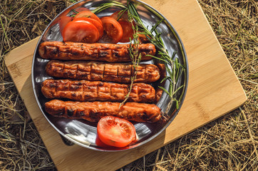 Sausages cooking on grill served on a plate with spices, herbs and tomatoes. Food background with barbecue party, top view