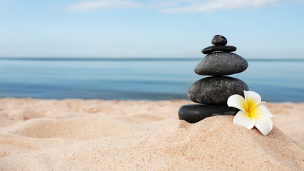 Stack of dark stones and flower on sand near sea, space for text. Zen concept