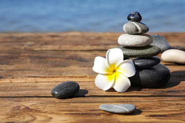 Fototapeta na wymiar Stack of stones and flower on wooden pier near sea, space for text. Zen concept