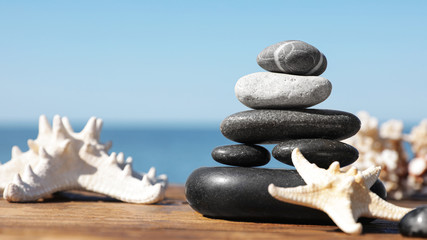 Stack of stones and starfishes on wooden pier near sea, space for text Zen concept
