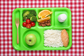 Serving tray with healthy food on checkered background, top view. School lunch
