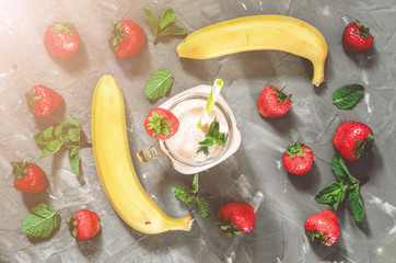 banana and strawberry smoothies with mint in a glass with a straw on the table, top view