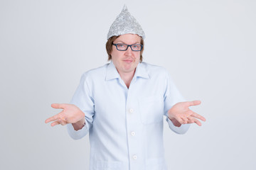 Young man doctor with tinfoil hat shrugging shoulders