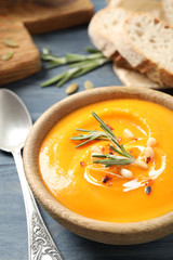 Delicious pumpkin soup in bowl on blue wooden table, closeup