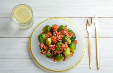 Flat lay composition of tasty roasted Brussels sprouts with bacon on white wooden table