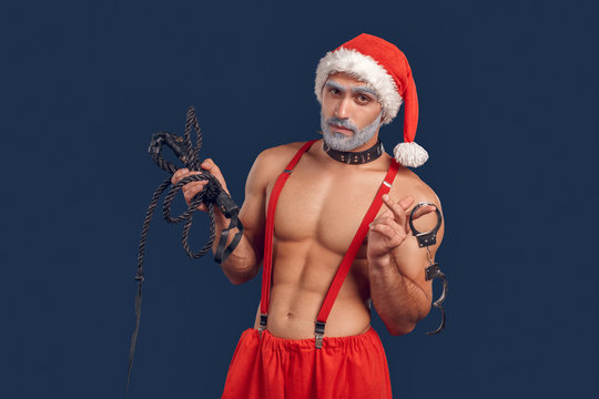 Adult Santa Claus standing with handcuffs and flogging whip in hands