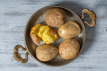 Baked potato in a metal bowl on a wooden table, simple vegetarian food. Boiled potatoes on wooden table, close up