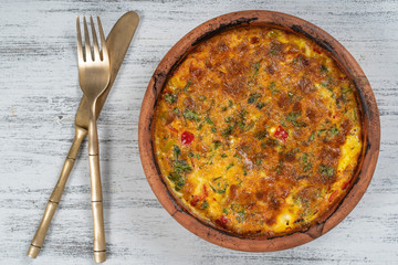 Ceramic bowl with vegetable frittata, simple vegetarian food. Frittata with tomato, pepper, onion and cheese on wooden table, close up. Italian egg omelette