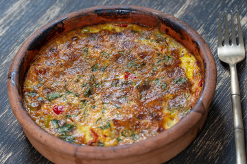 Ceramic bowl with vegetable frittata, simple vegetarian food. Frittata with tomato, pepper, onion and cheese on wooden table, close up. Italian egg omelette