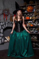 A beautiful, young girl in a black corset, a green skirt and a black hat. The image of a witch in halloween. A model with clean skin.