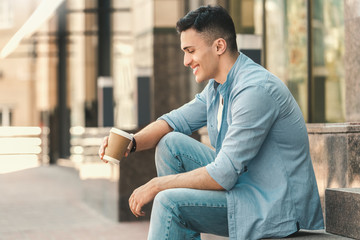 Outdoors Leisure. Stylish guy sitting on stairs on the street drinking hot coffee laughing happy side view