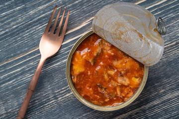 Open canned sprats in tomato sauce on a wooden background, closeup, top view
