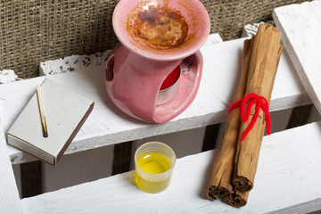 Aroma lamp stands on a wooden box. Nearby are oil in a cap and cinnamon sticks.