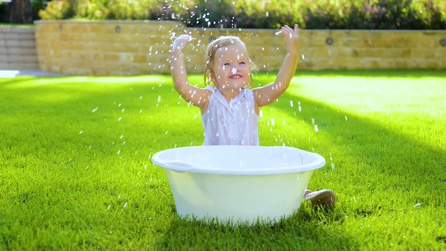 Outdoor baby bathing. Happy laughing baby taking a bath and playing outdoor. Girl in little basin