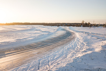Obraz premium An icy winding road on a frozen lake around which lies a lot of snow at sunset on a winter day. Snow race and drift season on cars.
