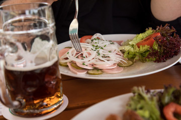 Mann mit dunklen Bier und Bayrischen Wurstsalat aus Stadtwurst, Zwiebel Ringe, saure Gurken und Schnittlauch im Biergarten