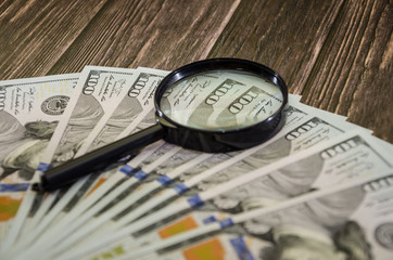 dollars and magnifier on a wooden background.