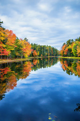 Fall foliage colors reflected in still lake water on a beautiful autumn day in New England
