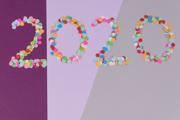 Inscription of 2020 number made of multicolored round confetti scattered on background made of gray and violer lines