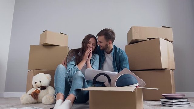 Appealing joyful pair in love sitting on the floor among many boxes in the new apartment and discussing interier's design