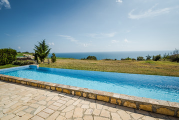 Outdoor swimming pool. Holiday villa exterior with a great scenery - green grass garden and an ocean 
