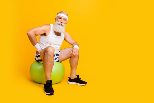 Full size photo of aged guy sitting on green fit ball after squats set making little break sportswear tank-top shorts sweatband sneakers isolated yellow color background