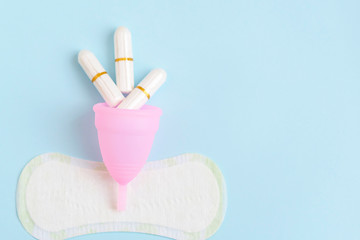pink menstrual Cup, tampons, pads on blue background. woman period concept.