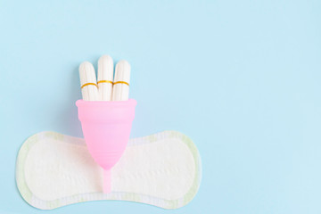 pink menstrual Cup, tampons, pads on blue background. woman period concept.