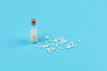 Gomeopathic globules in glass bottle on blue background.