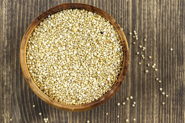Grain quinoa in a brown wooden bowl on a brown wooden background, top view