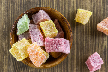 Turkish delight in a wooden brown bowl on a brown wooden background, top view