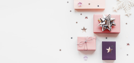 Banner with holiday presents. Gifts wrapped in pale pink and violet paper with silver ribbons and bow. Stars confetti and white copy space. Top view, flat lay.
