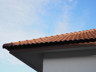 Top of house with roof tiles terracotta and blue sky background.