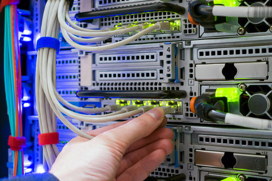 The hand of a technician with a communication Internet wire is a close-up. Connection of trunk cables to the network interface of the modern server. Service work in the datacenter server room.