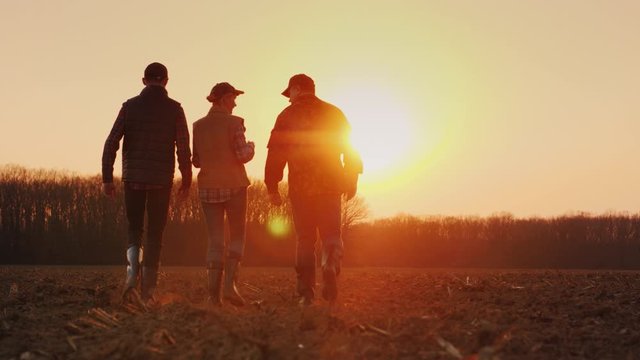 A group of young active farmers is moving forward along a plowed field towards the rising sun.