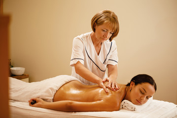 Obraz na płótnie Canvas Mature therapist massaging customer's back at spa salon.